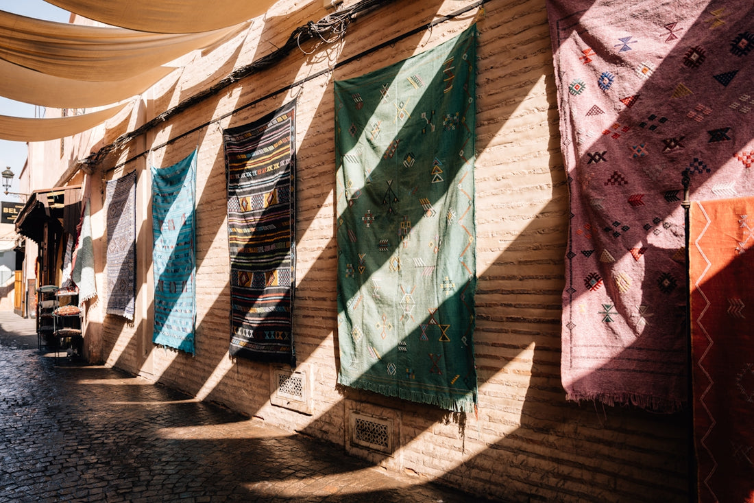 Textiles hang on a brick wall with striped shadows.