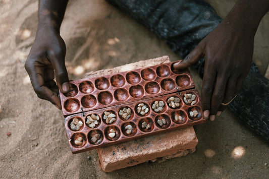 Hands holding a wooden mancala game board with seeds.